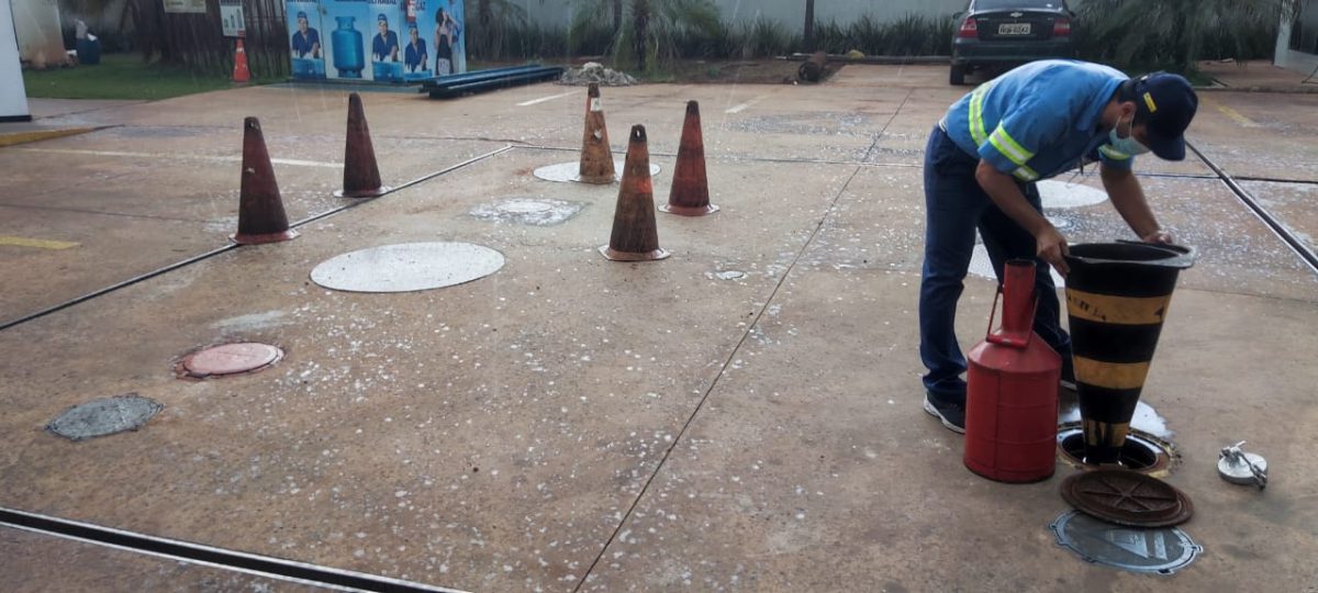 Frentista abaixado com cone na mão mexendo em reservatório. (Foto: Procon MS).